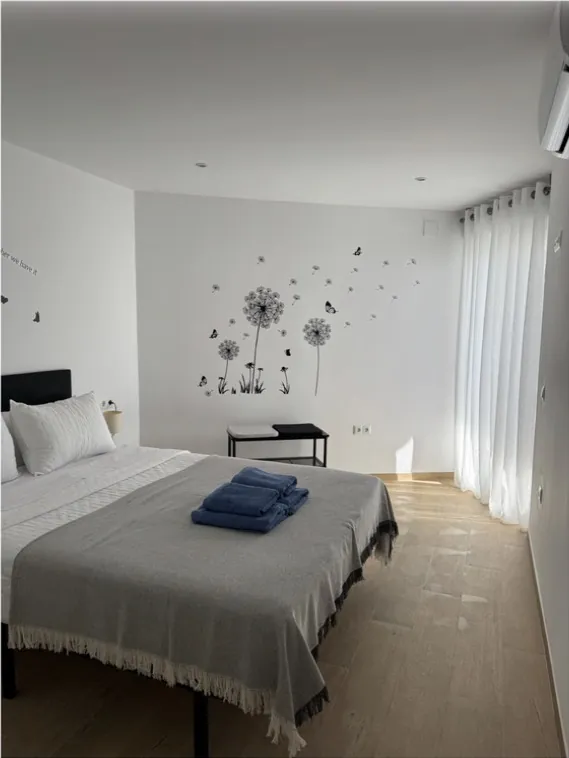 Dormitorio luminoso con colcha gris y toallas azules